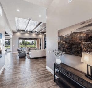 An open-concept entryway in a custom Easton Gray Development home, featuring a designer console table, a vaulted ceiling, and a view into a living area with a dramatic dark coffered ceiling and large sliding glass doors.