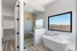 Luxury custom master bathroom showcasing a freestanding soaking tub beneath a large window, paired with a glass-enclosed shower and contemporary finishes in Arizona
