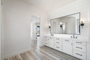 Spacious master bathroom vanity by Easton Gray Development, featuring clean white cabinetry with black hardware, a large framed mirror, and elegant wood-like tile flooring in Arizona