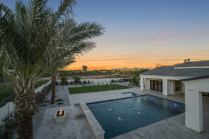 Luxury design-build backyard in Paradise Valley, AZ, featuring a custom swimming pool with an integrated spa, deck jets, and a modern fire pit lounge area at sunset.