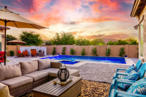 Luxury backyard design-build in Queen Creek, AZ, featuring a modern outdoor lounge with a sectional sofa, custom swimming pool, and professional landscaping at sunset.