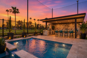 Luxury design-build backyard in Chandler, AZ, featuring a custom swimming pool, integrated outdoor kitchen with stone masonry, and a modern patio cover at sunset.