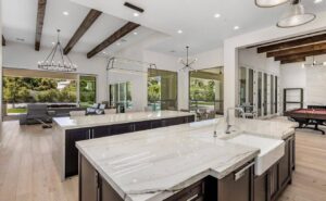 Modern Great room with vaulted wood-beamed ceilings, a large circular wagon wheel chandelier, and folding glass doors opening to a resort-style backyard.