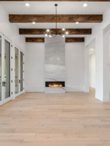 Luxury open-concept living room featuring a minimalist fireplace, exposed wood beams, and large white-framed glass doors.