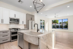 Luxury kitchen design with marble countertops, white cabinetry, stainless steel appliances, and a modern farmhouse sink, with unique geometric chandelier.